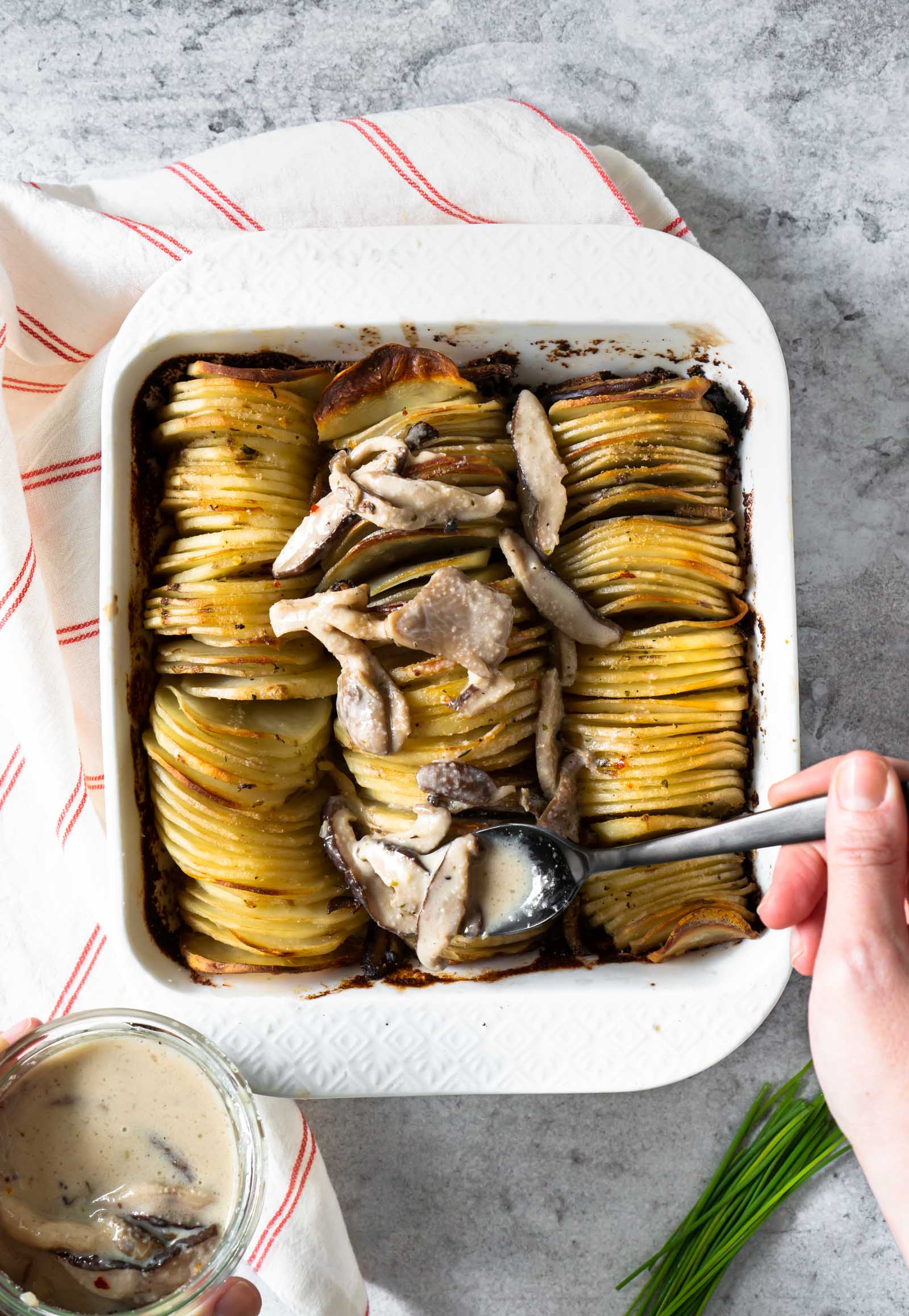 a black spoon putting creamy mushroom sauce over hasselback potato gratin