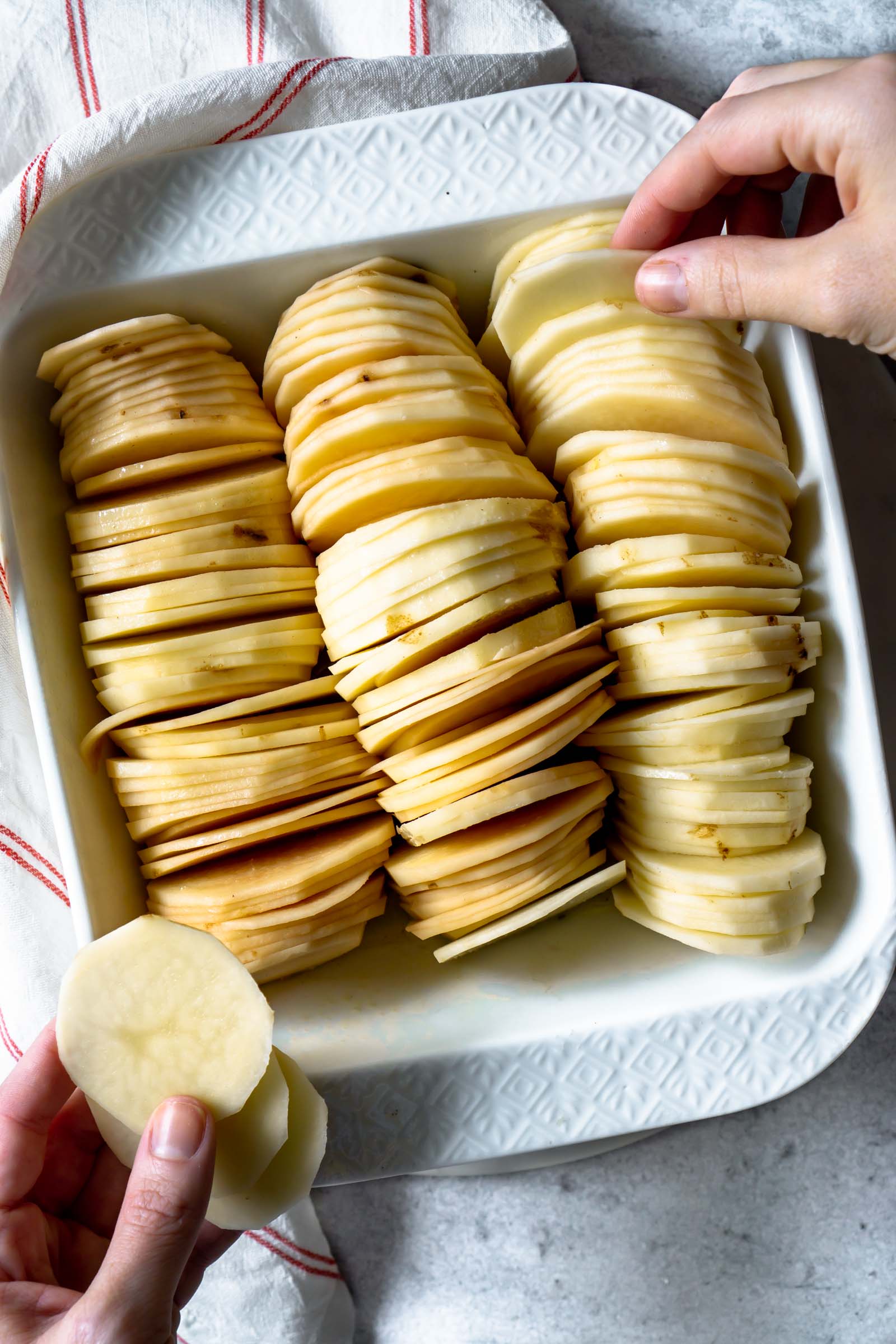 a hand placing potato slices in a baking dish