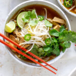 chicken pho in a white bowl with red chopsticks