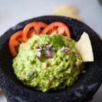 gaucamole with a chip and sliced tomatoes in a molcajete