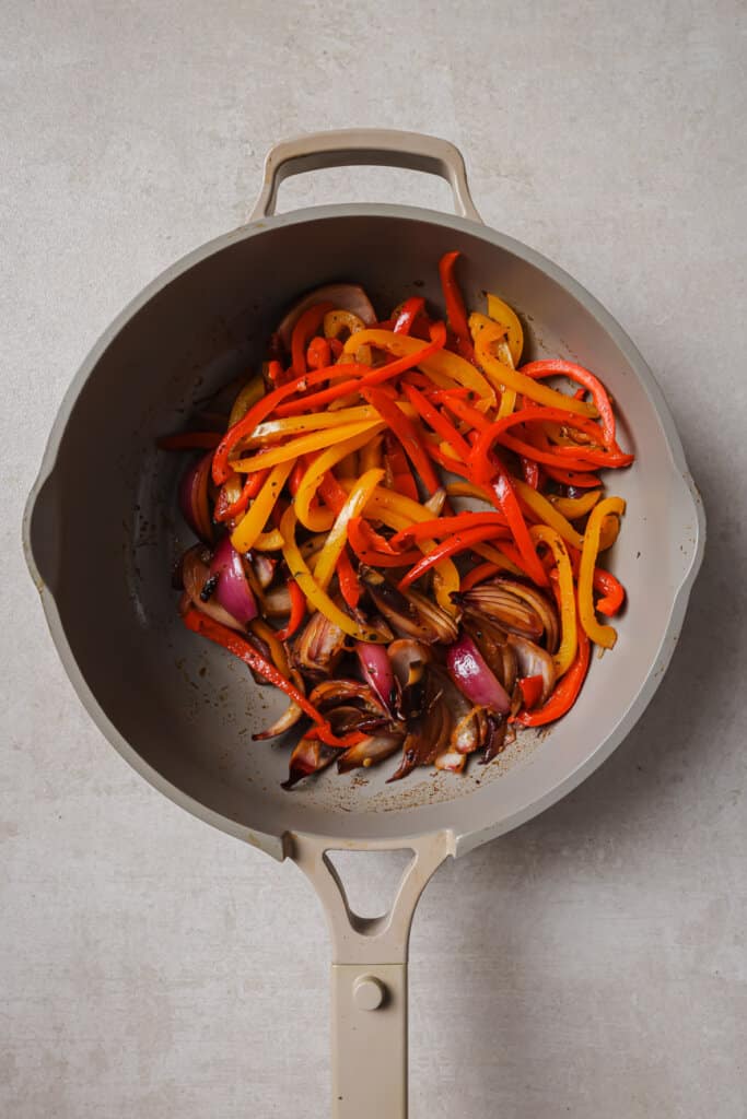 Adding peppers and onion to skillet with chicken.