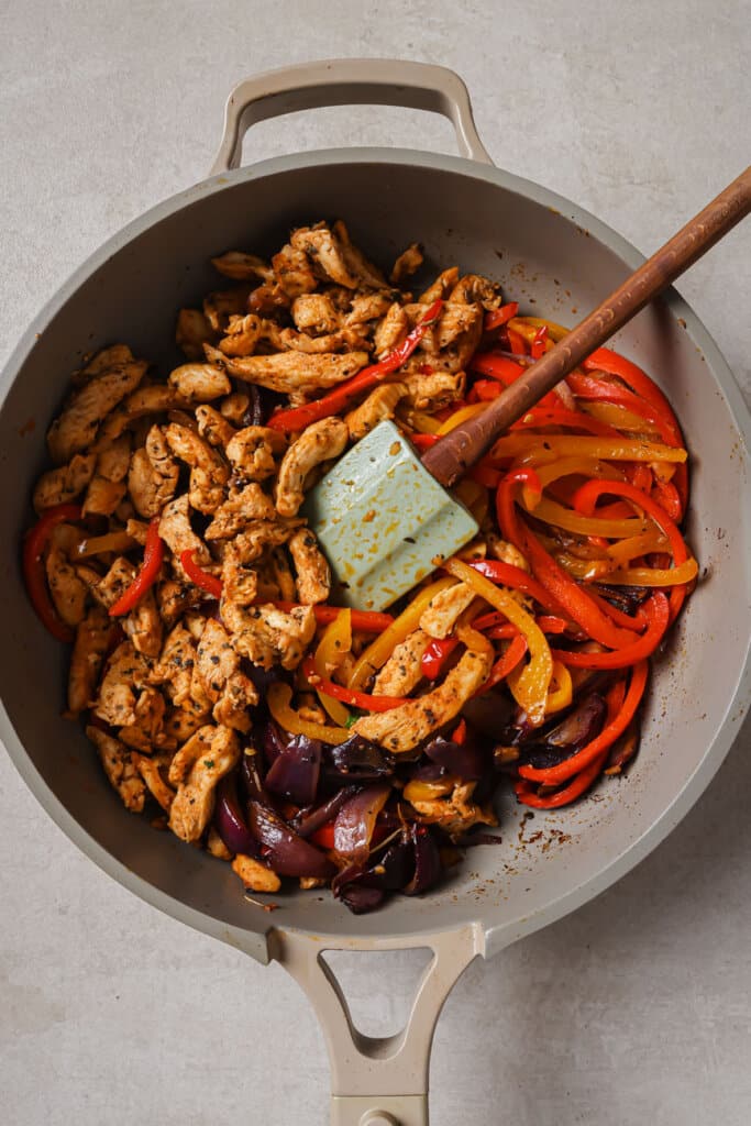 Mixing together chicken and peppers in a skillet.