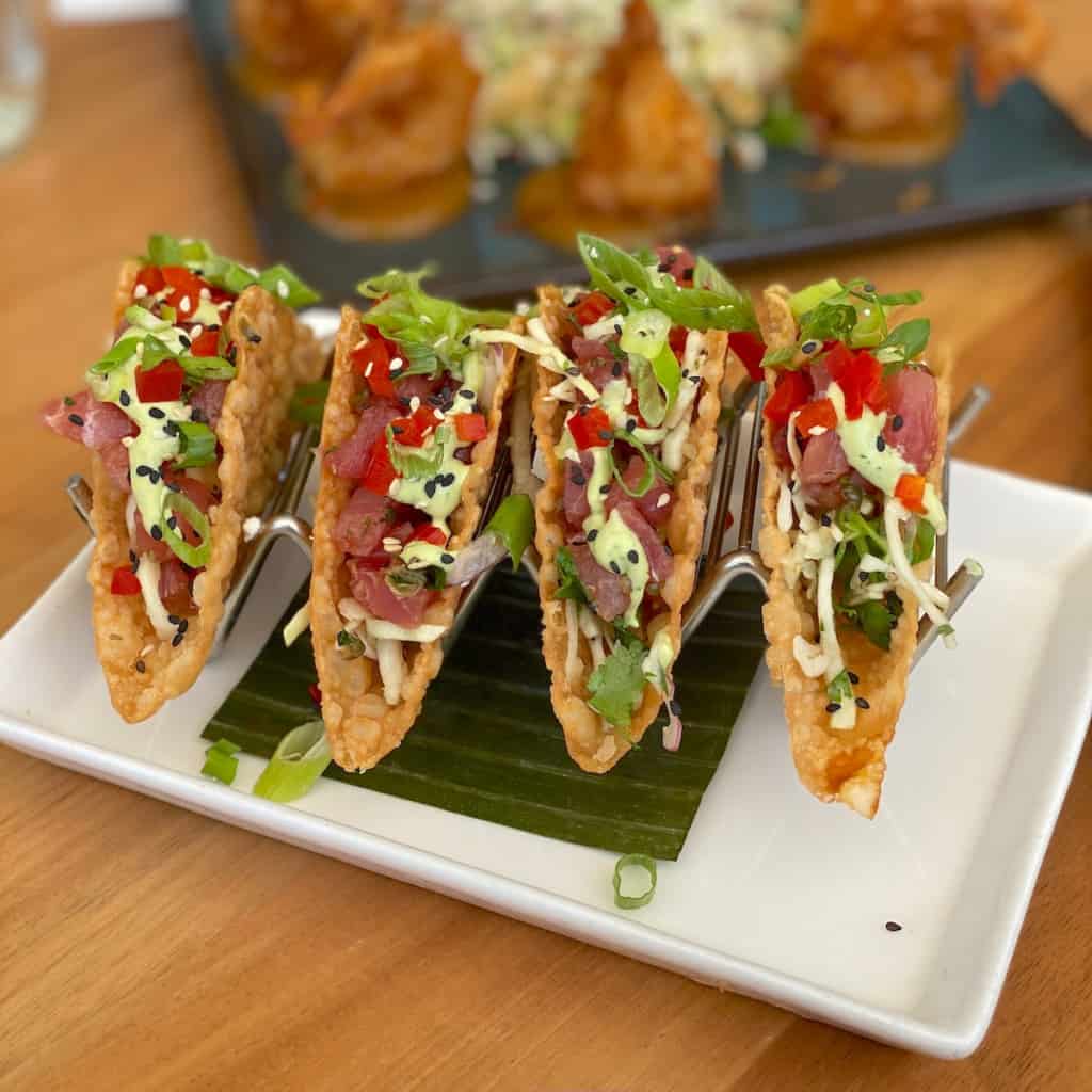 Tacos on a white plate set on a wood bar.