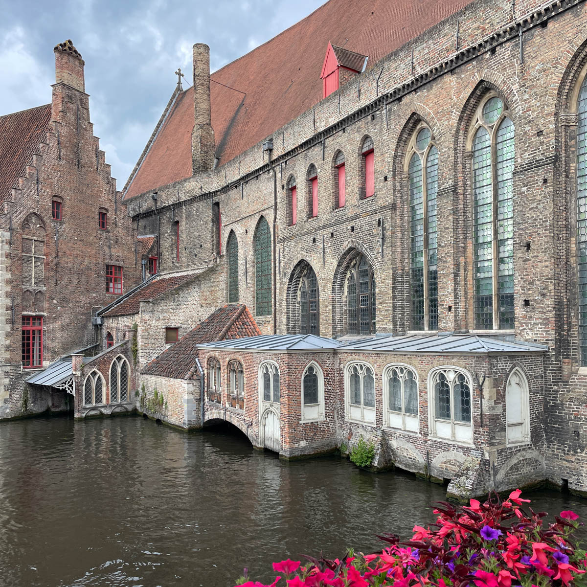 Historic building on a canal with flowers on railing of bridge.