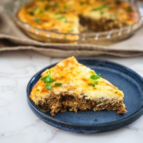 A slice of cheese and meat quiche on a plate.