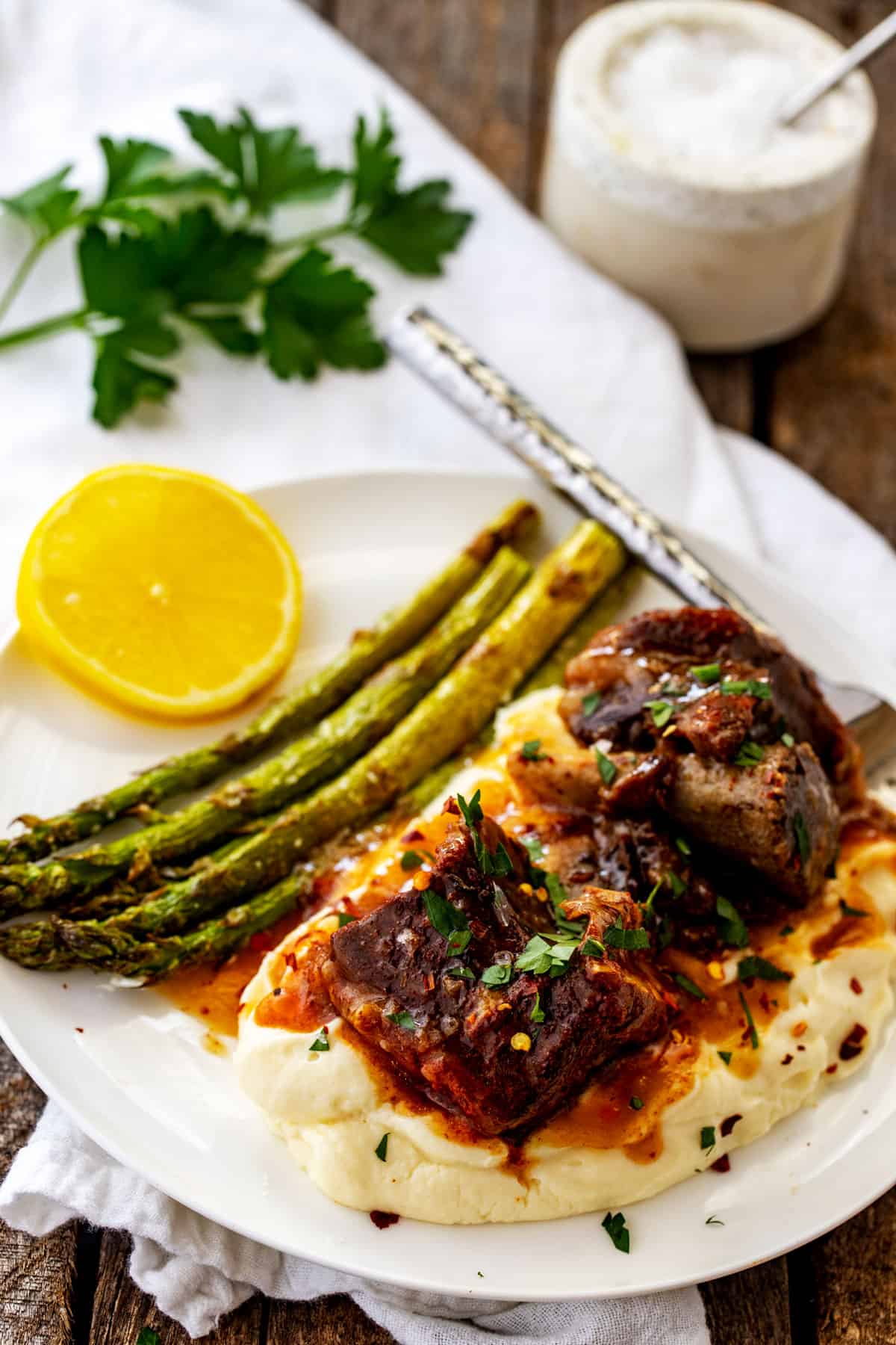 Photo of a white plat with Instant Pot Beef Ribs covered in gravy on a bed of mashed cauliflower.