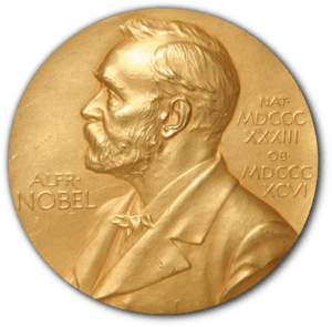 A golden medallion with an embossed image of a bearded man facing left in profile. To the left of the man is the text "ALFR•" then "NOBEL", and on the right, the text (smaller) "NAT•" then "MDCCCXXXIII" above, followed by (smaller) "OB•" then "MDCCCXCVI" below.