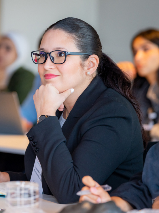 A woman wearing a black blazer and spectacles looking across.