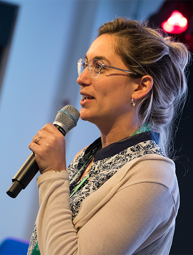 A woman speaking in a microphone while another woman is in soft focus.