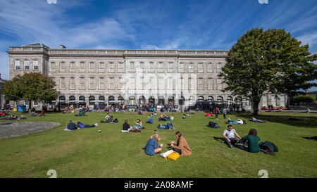 Students relaxing and ejoying a leisurely day with beautiful weather on the lawn outside The Book of Kells, Trinity Old Library in Dublin, Ireland. Stock Photo