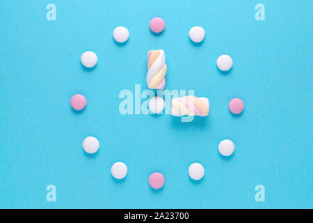 concept image, a clock with candy and marshmallow on blue Stock Photo