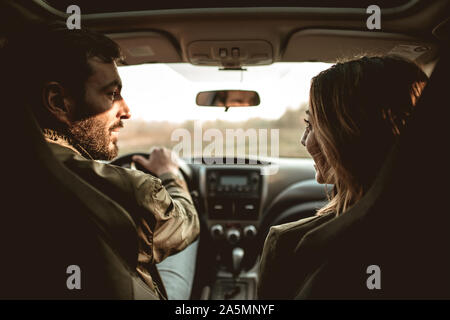 Rear view of young beautiful couple sitting on front passenger seats and looking at each other. Stock Photo