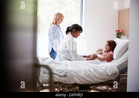 Female Doctor Visiting Mother And Daughter Lying In Bed In Hospital Ward Stock Photo