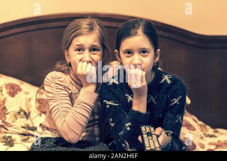 people, children, television, friends and friendship concept - two scared little girls watching horror on tv at home. toned. Stock Photo