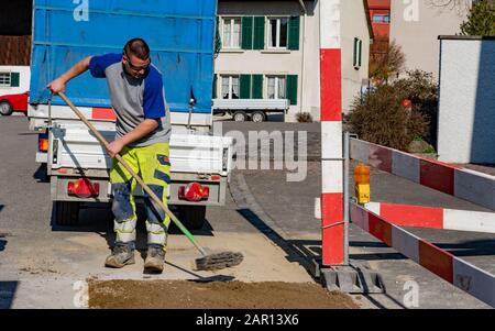 Pipeline mechanic with broom is scrubbing sand in construction site in front of a construction vehicle and trailer. Stock Photo