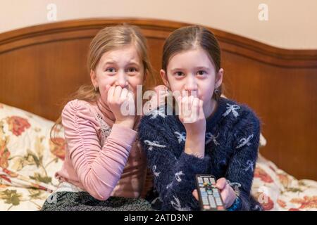 people, children, television, friends and friendship concept - two scared little girls watching horror on tv at home. toned. Stock Photo