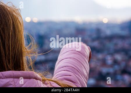 Girl with brown hair and pink jacket pointing in distance towards city Stock Photo