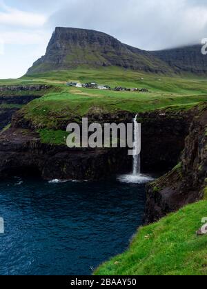 Faroe Islands, famous Mulafossur Waterfall, its water falling into the ocean. Above there is a village Gasadalur. Stock Photo