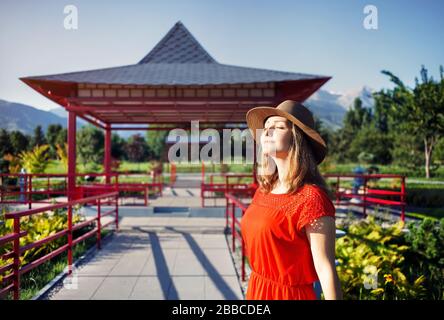 Portrait of beautiful woman in orange dress and hat near the pagoda in Japanese Garden Stock Photo