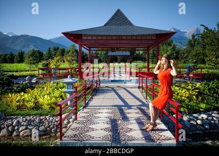 Portrait of beautiful woman in orange dress and hat near the pagoda in Japanese Garden Stock Photo