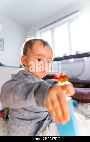 Portrait of one year old baby girl indoors in bright room playing by herself Stock Photo