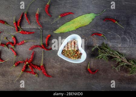 studio shot of assorted spices with whole red peppers rosemary and allium ursinum with melted mixture of them in heart shaped white bowl  on wooden bo Stock Photo