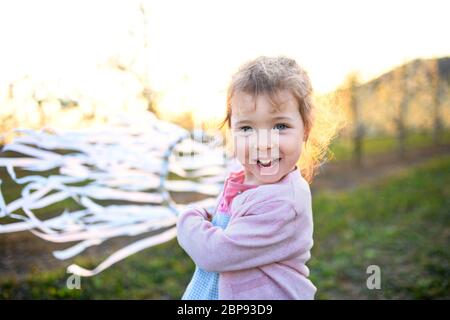 Small toddler girl standing outdoors in orchard in spring, holding hand ribbon ring. Stock Photo