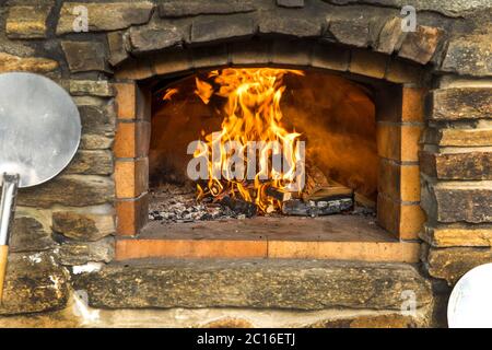 Old stone homemade pizza oven. Fire in the furnace. Homemade baking pizza. Bakery. Traditional Italian food. Stock Photo