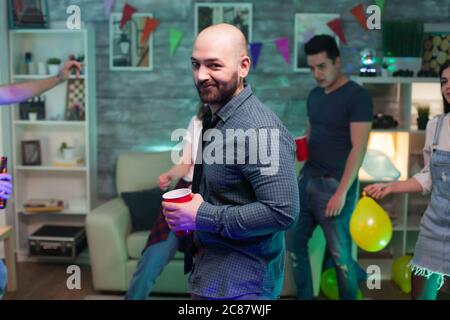 Bald man looking at the camera at a party his friends while partying. Man standing with a beer cup. Stock Photo