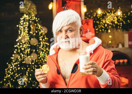 Christmas for modern Santa Claus. Santa make funny face and picking cookie. Santa Claus eating cookies and drinking milk on Christmas Eve. Christmas Stock Photo