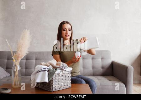 Woman pouring detergent into bottle lid. She is sitting at table with clothes collected in the basket Stock Photo