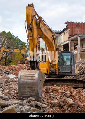 Yellow excavator at demolition site, destroyed old building at background Stock Photo