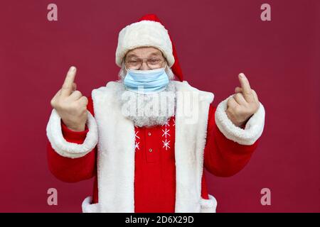 Santa Claus wearing face mask showing middle fingers on red background. Stock Photo