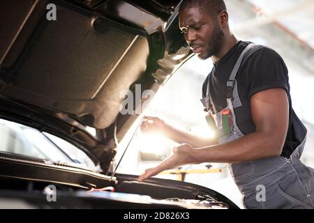 repairing in action. hardworking guy employee in uniform works in the automobile salon, confident auto mechanic is professional worker of service Stock Photo