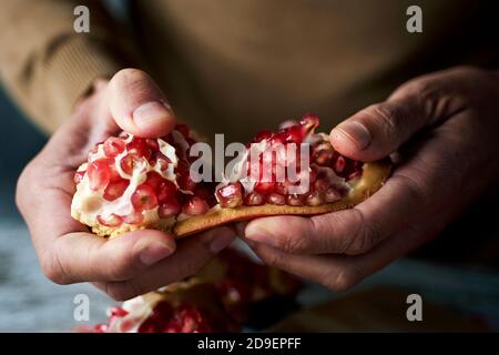 closeup of a young caucasian man, wearing a brown pullover, opening a pomegranate fruit on a rustic wooden table Stock Photo