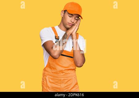 Young handsome african american man wearing handyman uniform sleeping tired dreaming and posing with hands together while smiling with closed eyes. Stock Photo