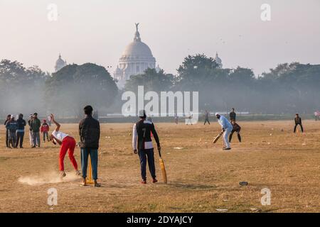 Boys playing cricket at Kolkata Maidan area on a foggy winter morning with view of Victoria Memorial monument in the backdrop Stock Photo