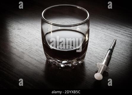 Glass of the Whiskey and a Syringe on the Table in the Dark Room Stock Photo