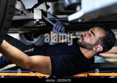 Side view of male technician lying on car creeper and screwing part of automobile wheel with metal spanner in modern service Stock Photo