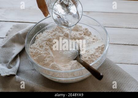 Hand pouring water over flour in a bowl for making bread dough. Homemade bread Stock Photo