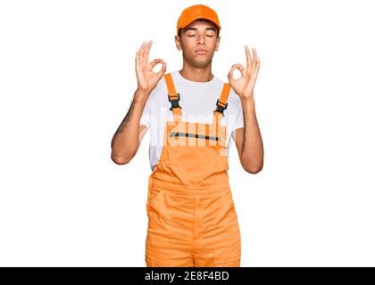 Young handsome african american man wearing handyman uniform relax and smiling with eyes closed doing meditation gesture with fingers. yoga concept. Stock Photo