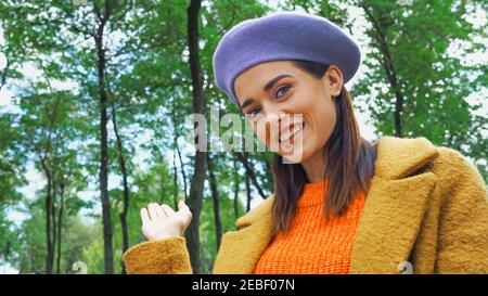 smiling woman pointing with hand while looking at camera in park Stock Photo