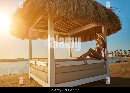 Woman sitting at Cabana with straw roof on a sandy beach on sunset Stock Photo