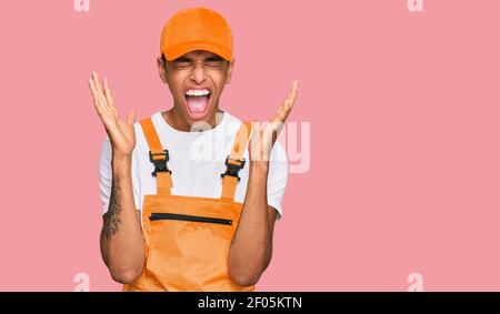 Young handsome african american man wearing handyman uniform celebrating mad and crazy for success with arms raised and closed eyes screaming excited. Stock Photo