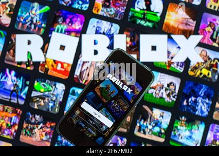 In this photo illustration, the Roblox app seen displayed on a smartphone screen and a Roblox logo in the background. Stock Photo