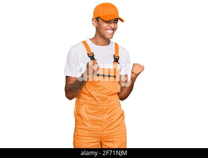 Young handsome african american man wearing handyman uniform excited for success with arms raised and eyes closed celebrating victory smiling. winner Stock Photo