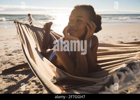 Happy african american woman lying in hammock on beach looking ahead Stock Photo