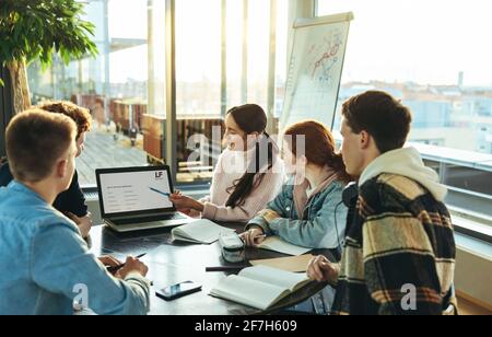 Girl student explaining presentation on laptop to classmates in college. Young female showing laptop to her friends during group study in high school. Stock Photo