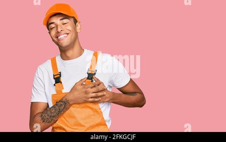 Young handsome african american man wearing handyman uniform smiling with hands on chest with closed eyes and grateful gesture on face. health concept Stock Photo