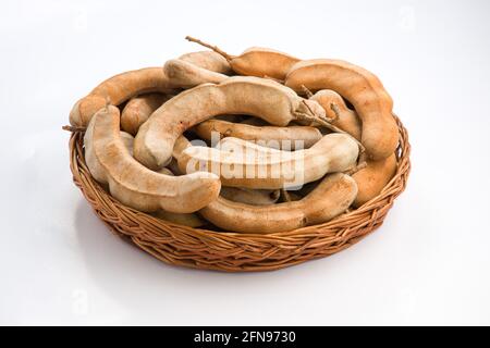 Tamarind  bean like pods filled with seeds surrounded by a fibrous pulp arranged in a basket with white textured background. Stock Photo